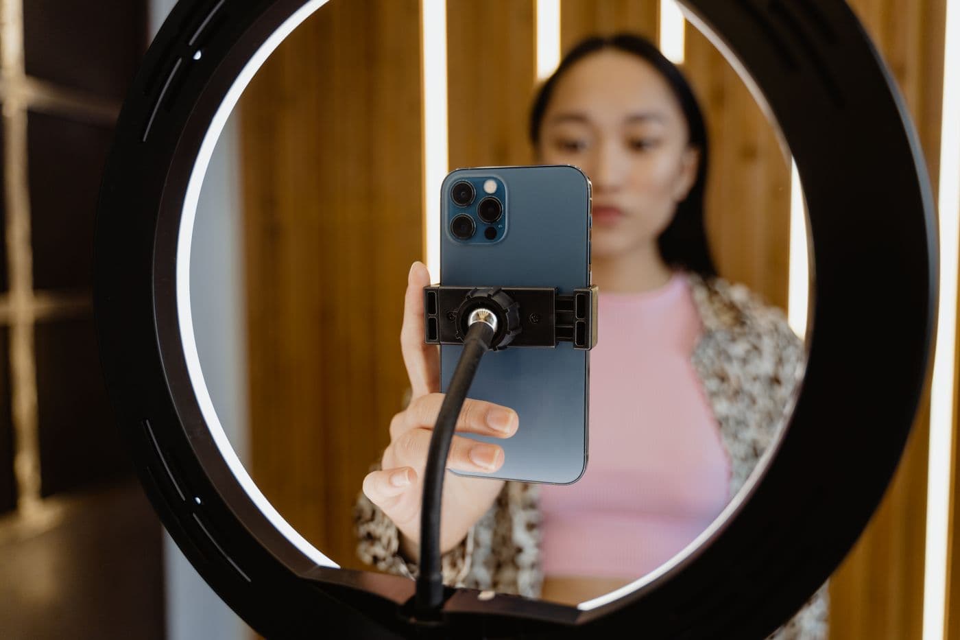 Perempuan memegang ponsel yang terpasang di tengah ring light untuk membuat konten